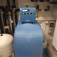 A képen egy modern épületgépészeti berendezés látható, amely a HydroArt Kft. terméke. A berendezés kék színű, és a falon különböző csövek és szelepek találhatók, amelyek az épületgépészethez kapcsolódnak. Az Öskü városában működő cég innovatív megoldásokat kínál az épületek hatékony működtetéséhez.